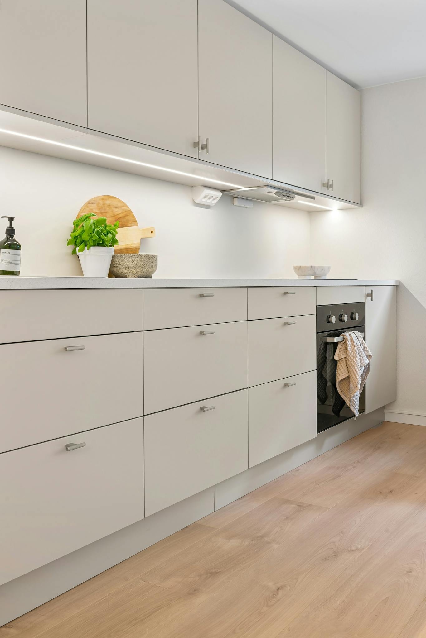 Bright and clean modern kitchen with white cabinetry, wooden flooring, and minimalist decor.