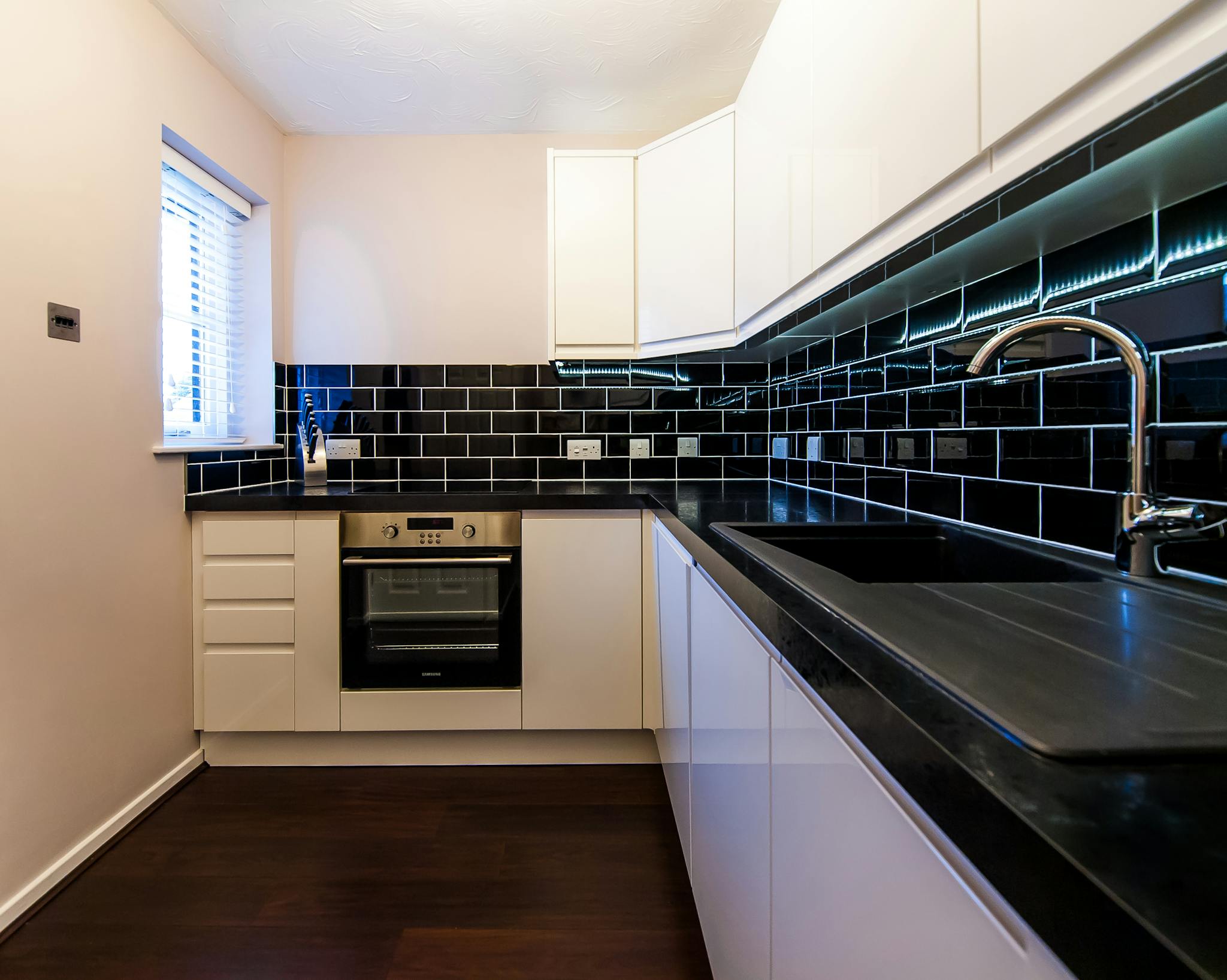 Sleek minimalist kitchen with black tiles and white cabinets in a London apartment.