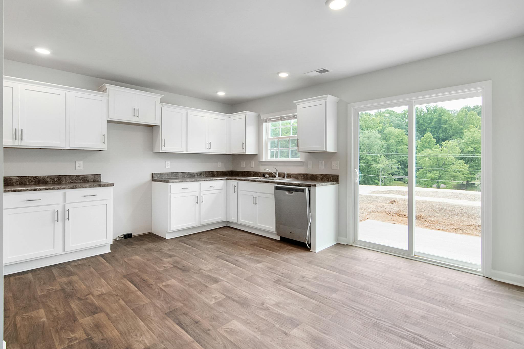 Spacious modern kitchen with white cabinets and a view of lush greenery.
